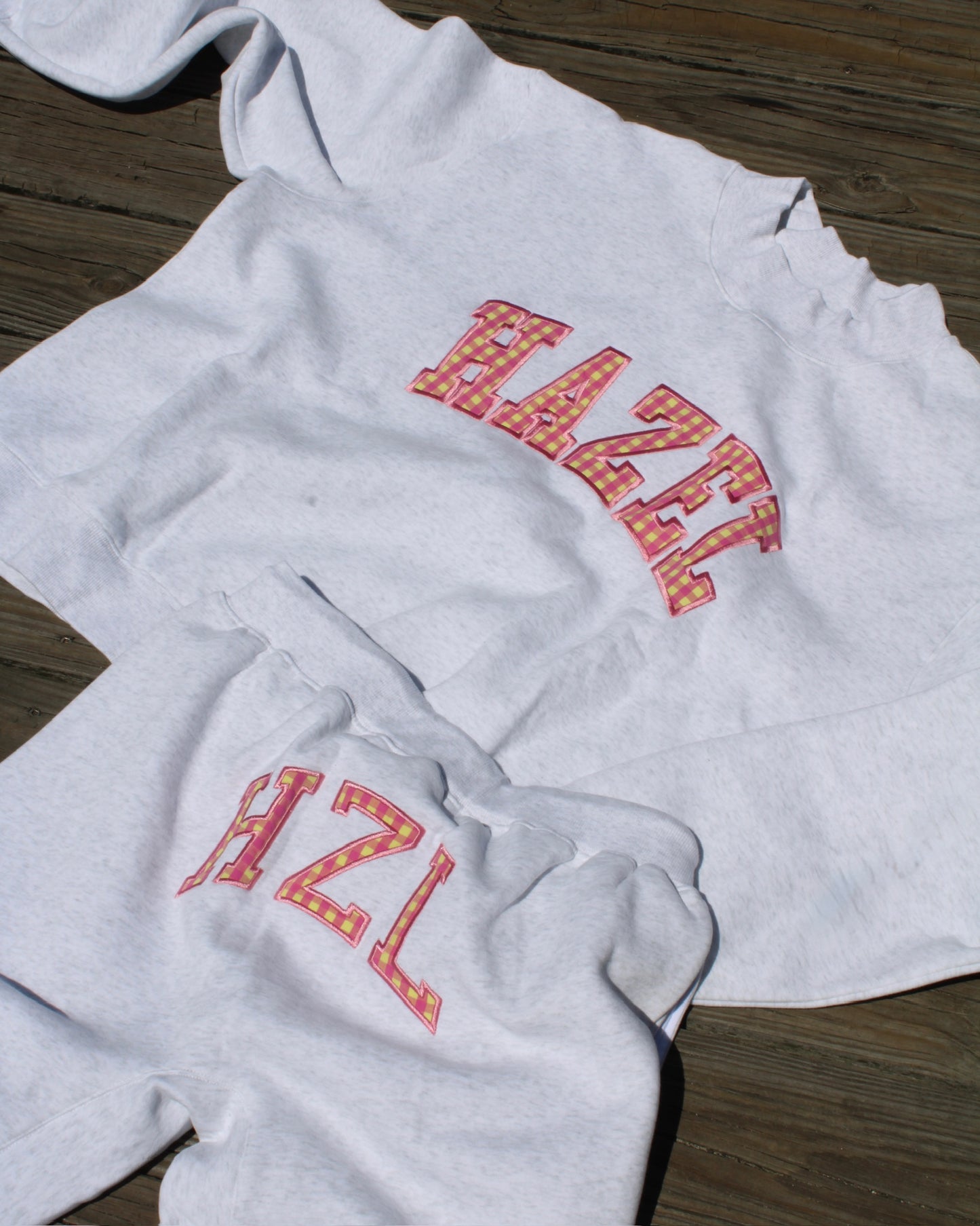 Light gray casual sweatshirt and pants set with colorful patterned "HAZL" lettering, laid out on wooden floor.