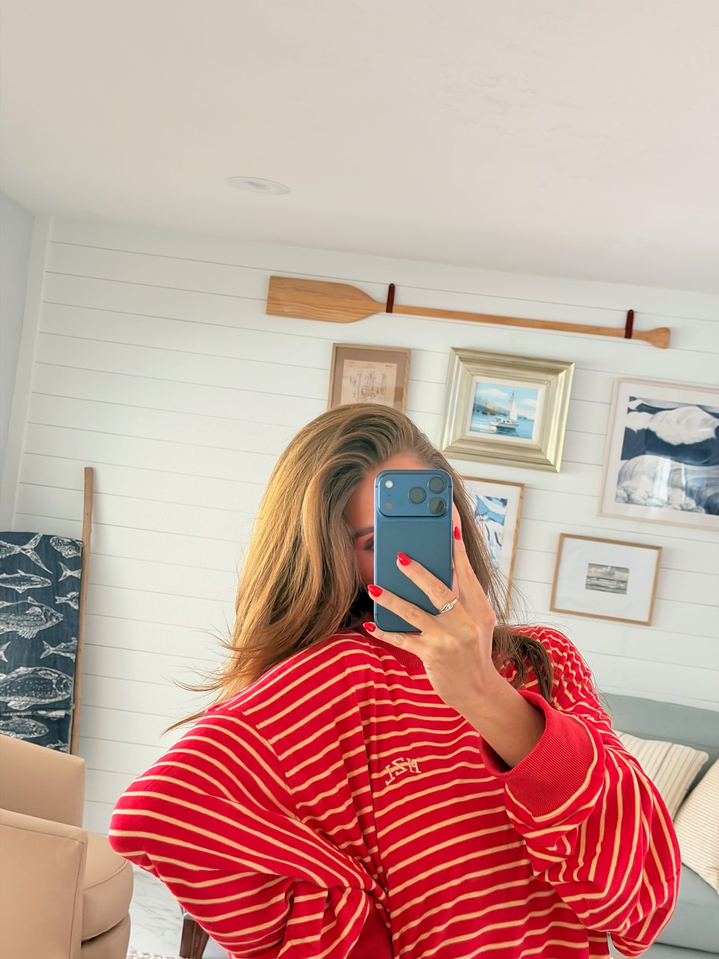 Woman taking a mirror selfie wearing a bold red striped mockneck top in a cozy nautical-themed room.