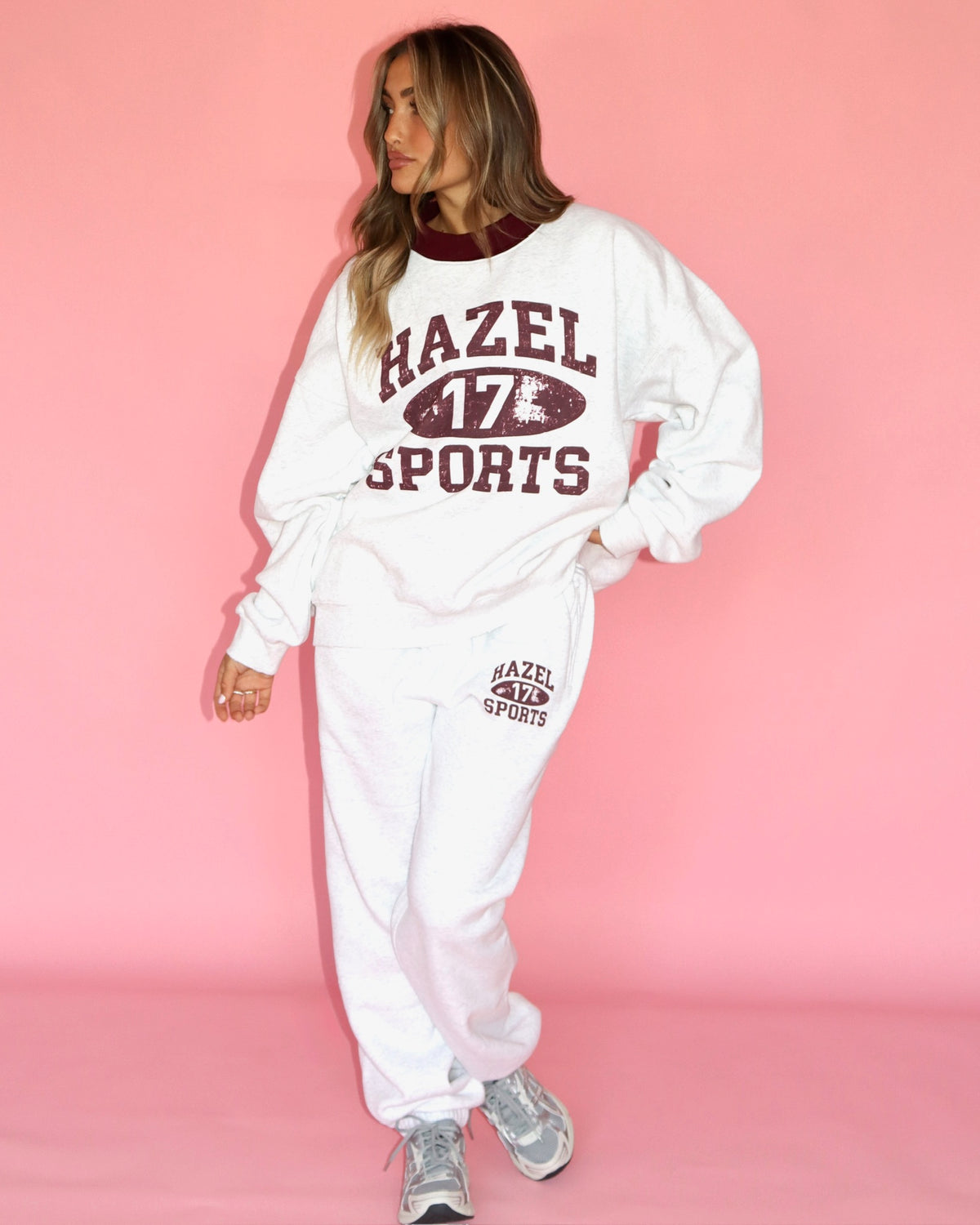 Model wearing a white sports sweatshirt and joggers with a 17 football graphic against a pink backdrop