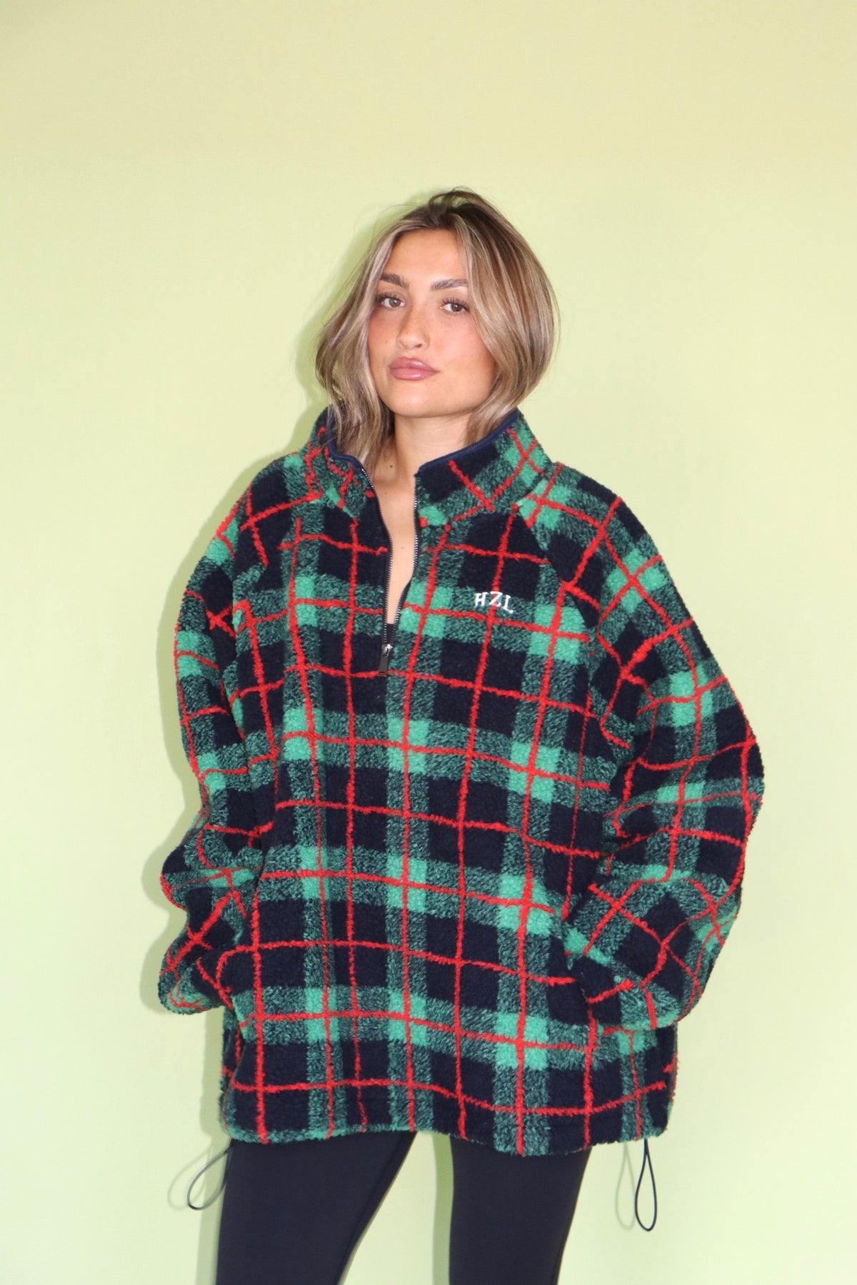 Model wearing a cozy green and red plaid fleece jacket with a zip front and high collar