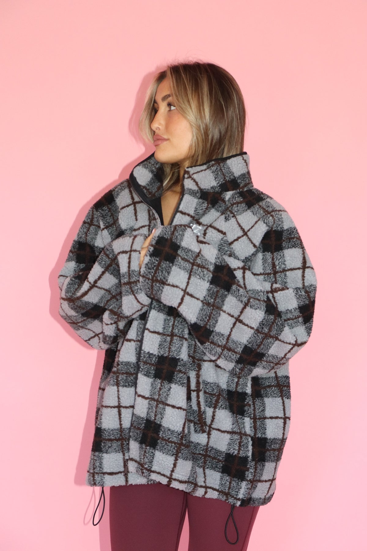 Woman wearing a gray and black plaid fleece jacket against a pink background