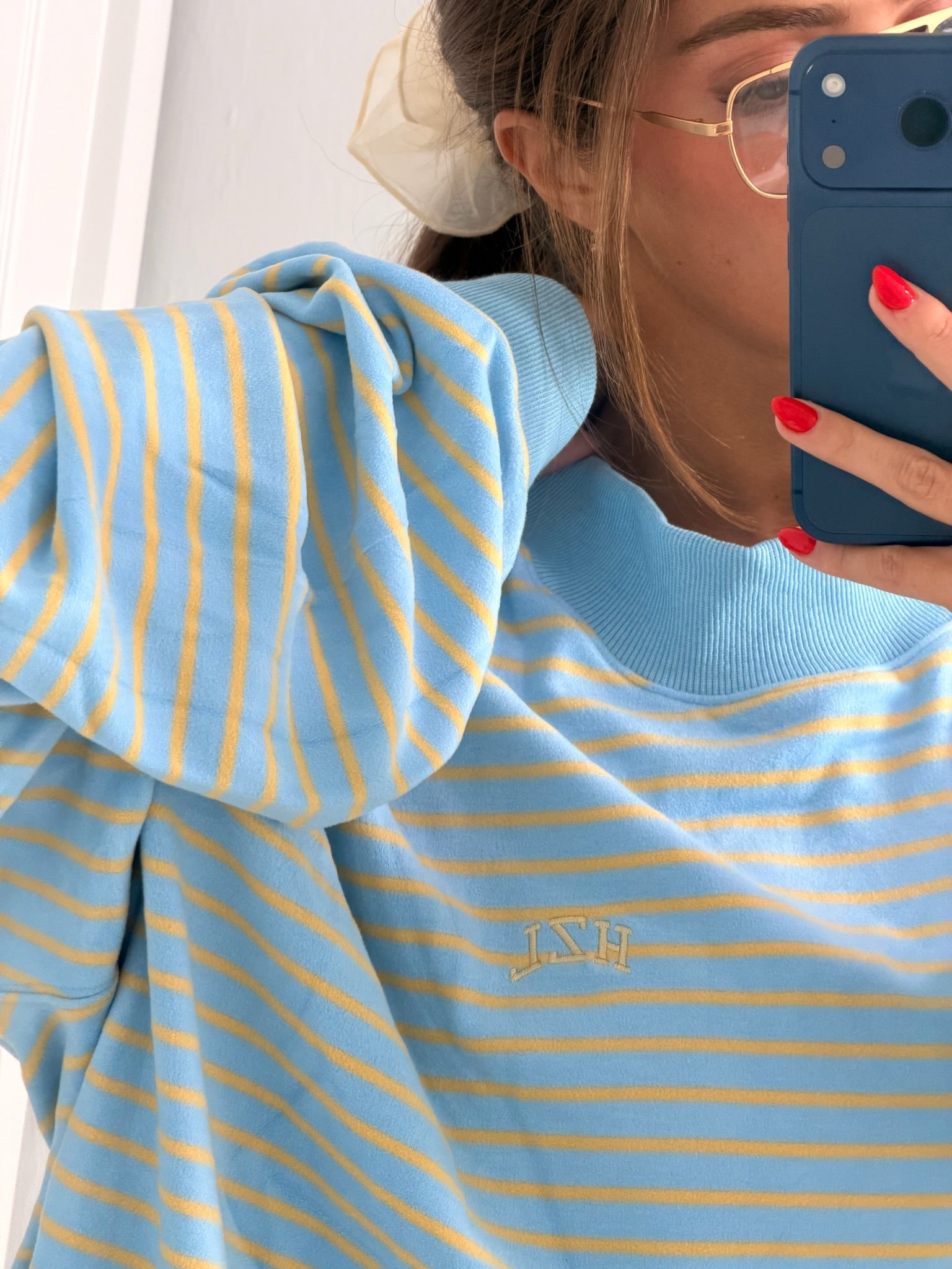Close-up of a person wearing a light blue and yellow striped sweatshirt with subtle embroidered lettering, casual and cozy style.