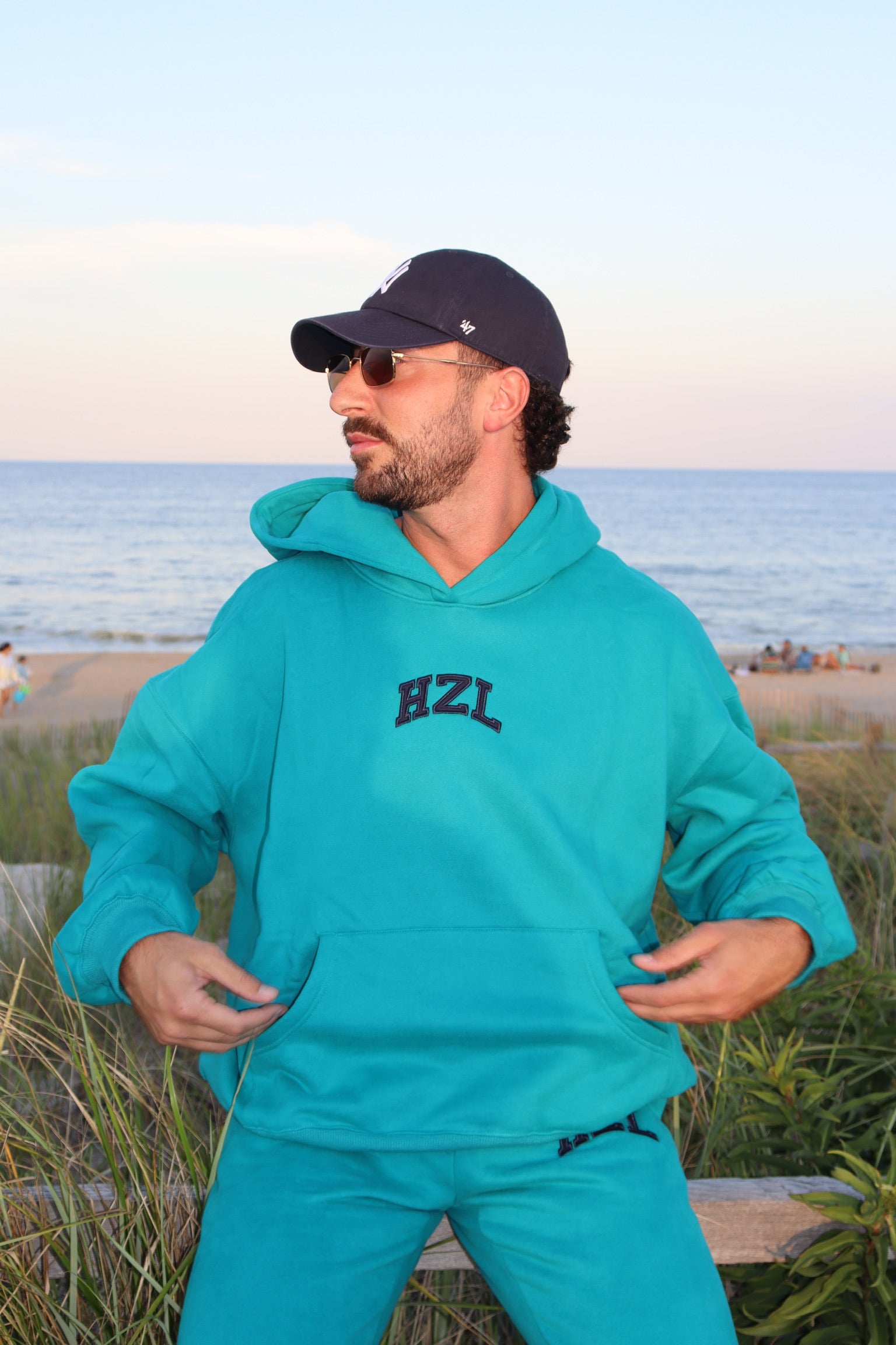 Man wearing a turquoise HZL hoodie and matching pants by the beach
