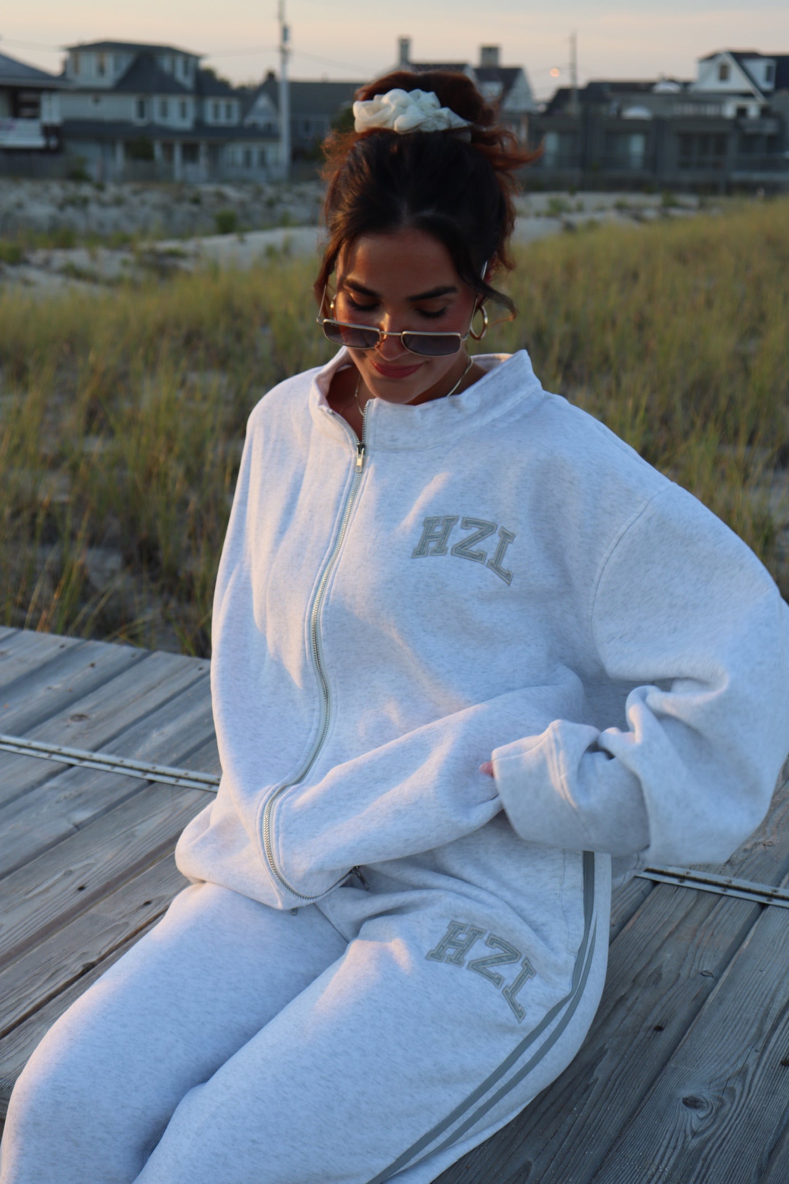 Woman wearing gray HZL sweatpants and matching zip hoodie seated on a beach boardwalk