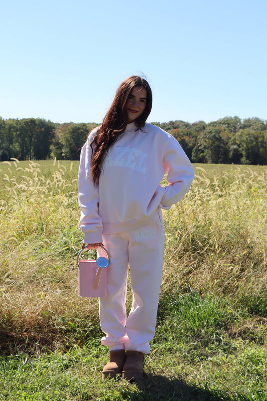Woman modeling pastel pink joggers with a matching sweatshirt in a sunny grassy field