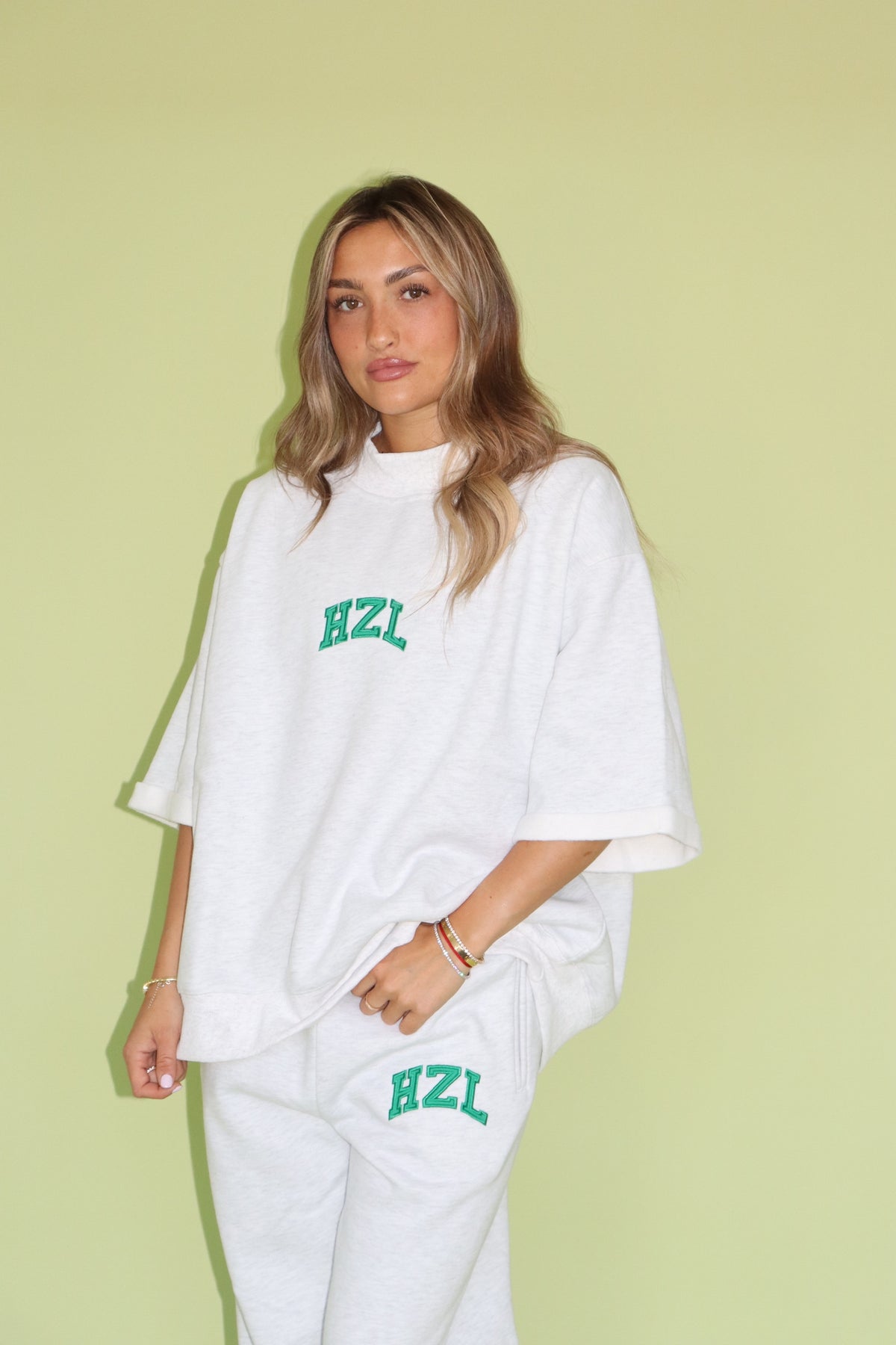 Model wearing a white HZL short sleeve mockneck top and matching pants with green lettering
