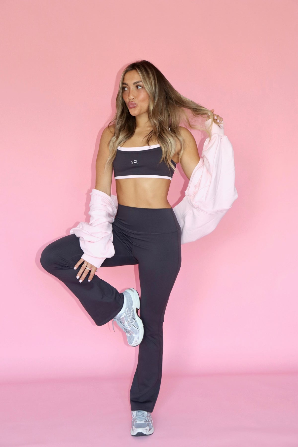 Model wearing slate grey bell bottom pants with a cropped athletic top and pink jacket