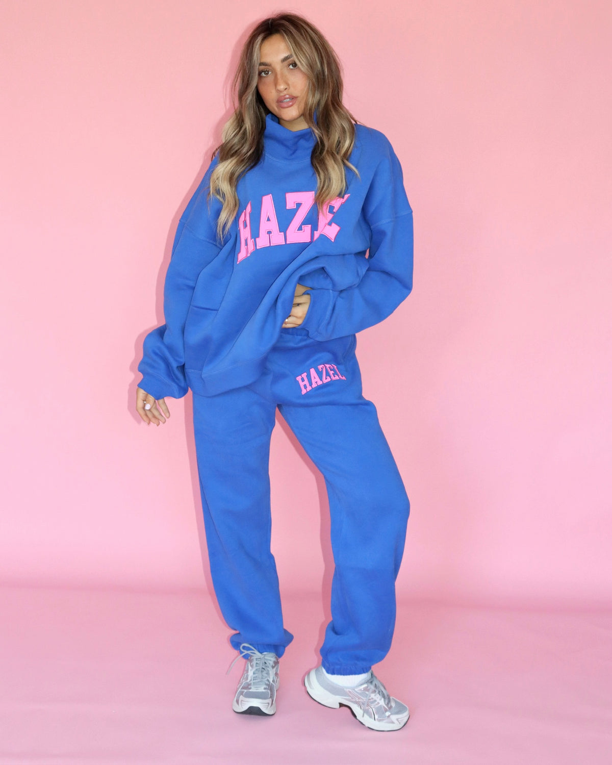 Model wearing blue HZL joggers and a matching hoodie with pink lettering against a pink backdrop