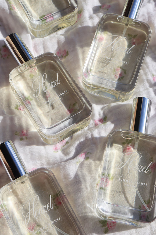 Hazel Summer Nights perfume bottles arranged on soft floral fabric in natural light