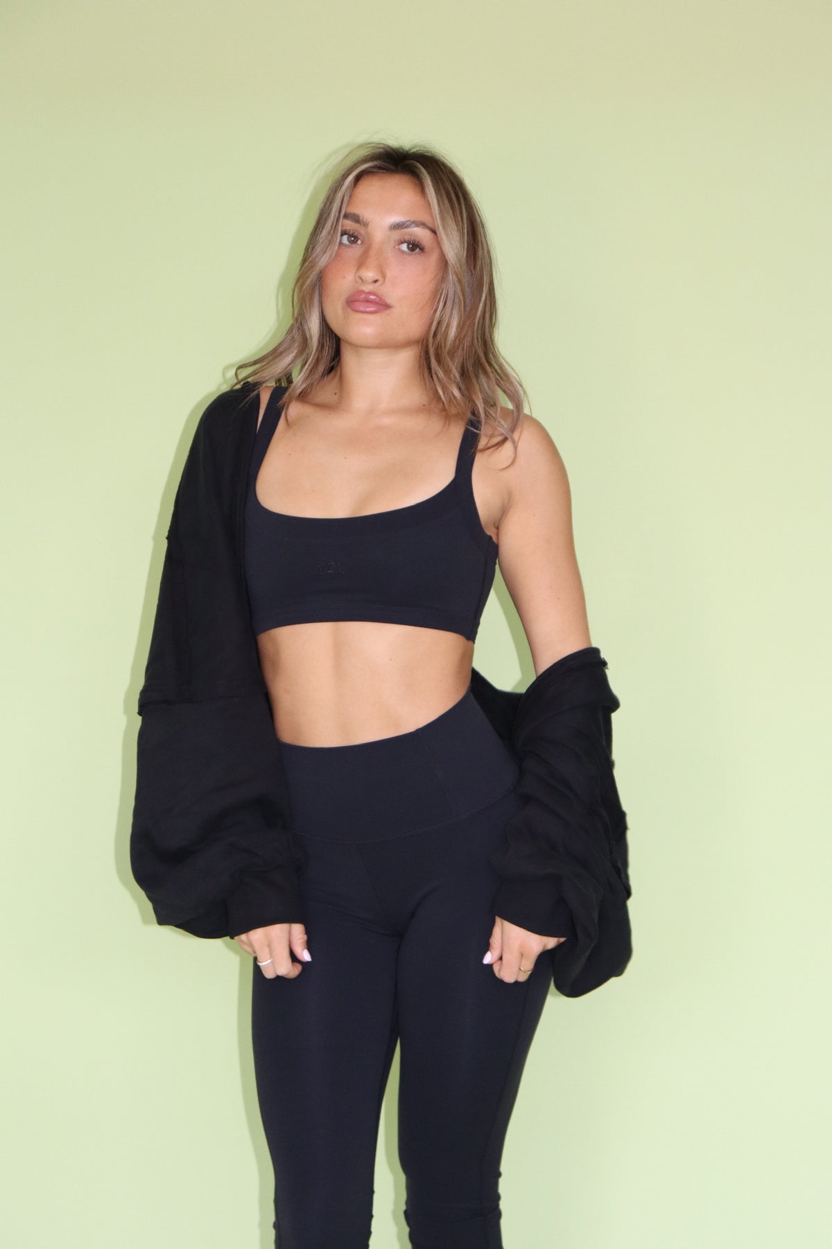 Model wearing a black scoop neck bra top with matching leggings and a draped jacket