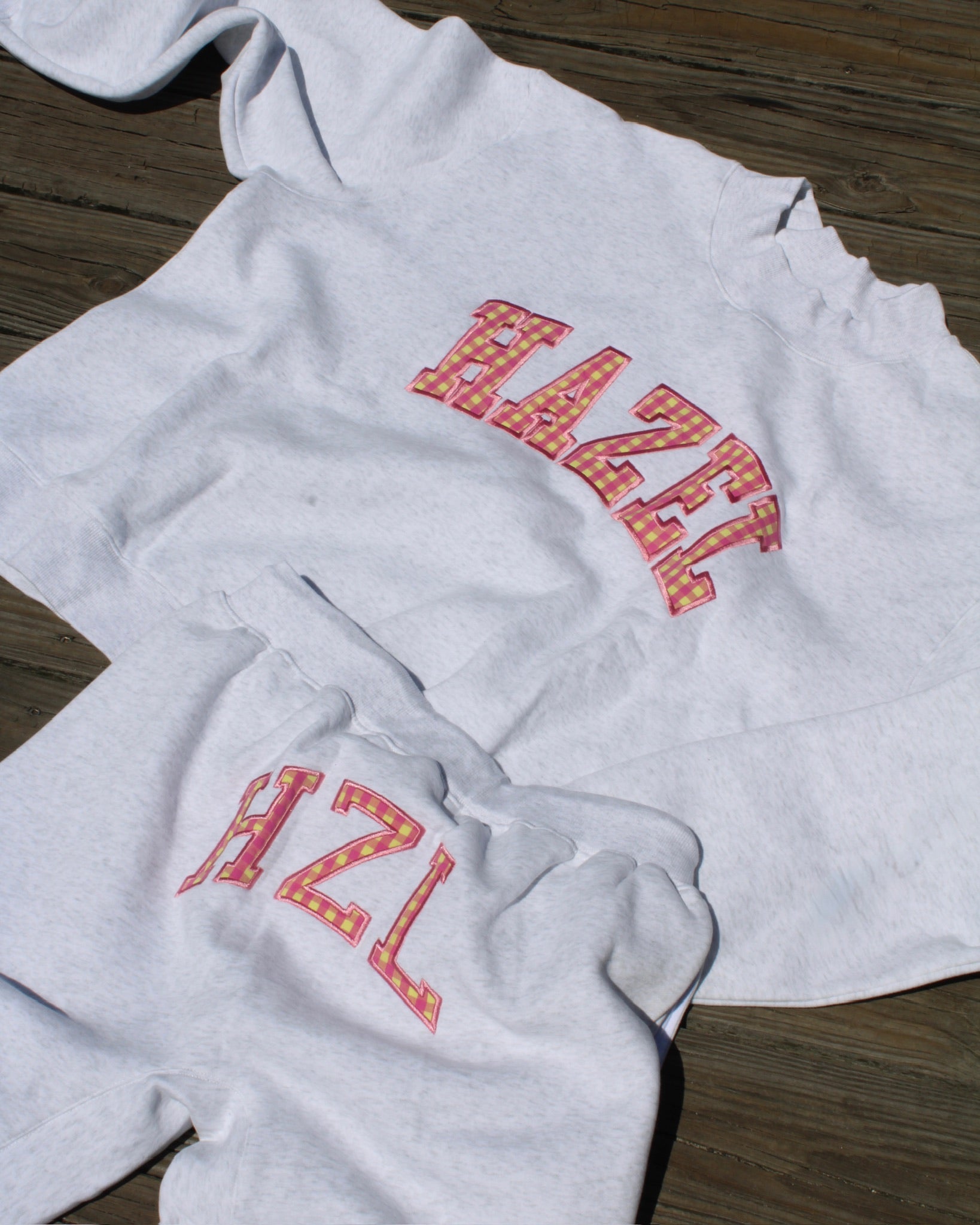 Light gray casual sweatshirt and pants set with colorful patterned "HAZL" lettering, laid out on wooden floor.