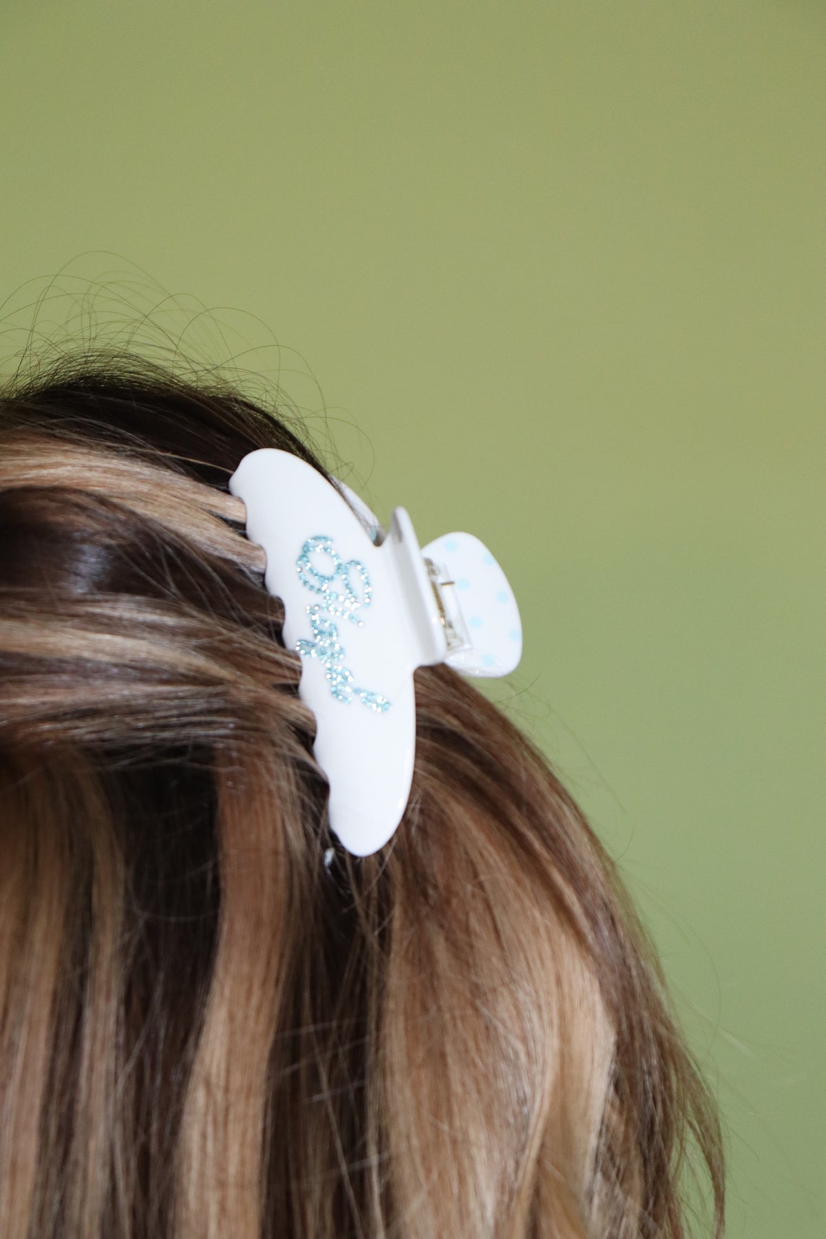 White claw hair clip with blue polka dot detail securing long brown hair