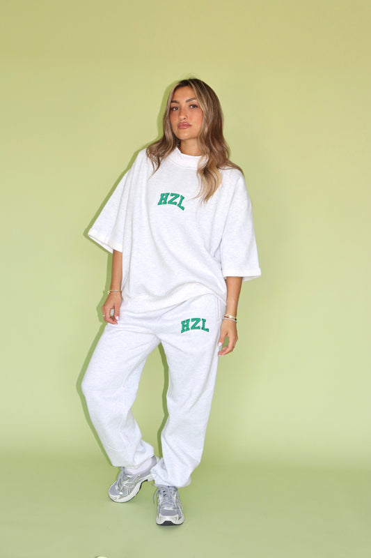 Model wearing white HZL joggers and an oversized tee with green logo against a pastel green backdrop
