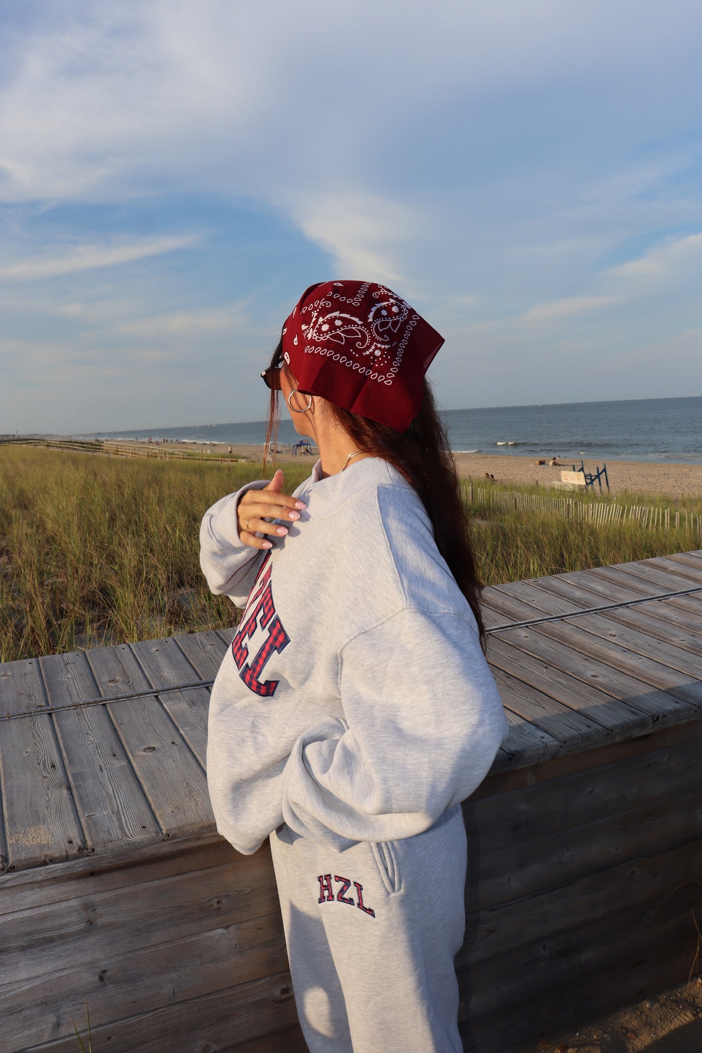 Woman wearing gray HZL joggers and sweatshirt with a red bandana on a beach boardwalk