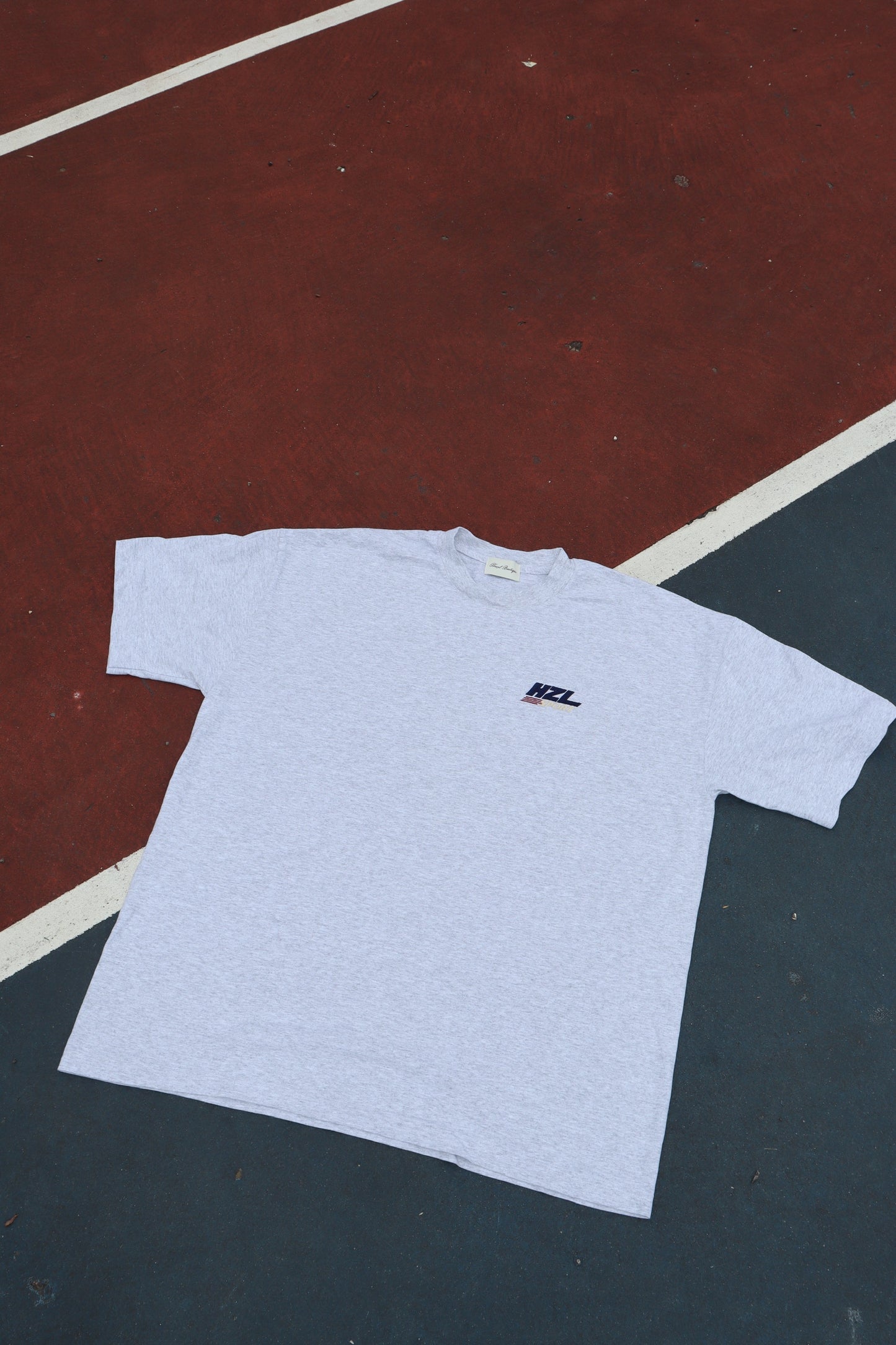Light grey T shirt laid flat on a court with a small HZL chest logo