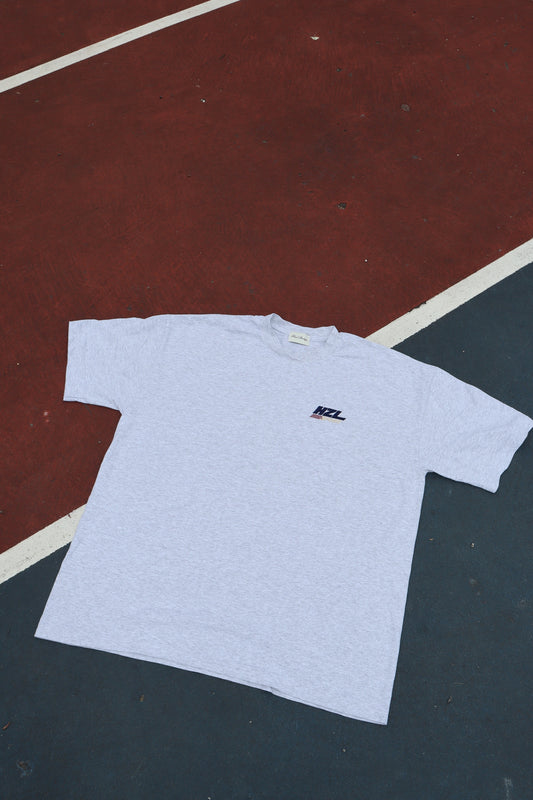 Light grey T shirt laid flat on a court with a small HZL chest logo