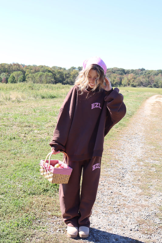 Model wearing brown HZL Charley barrel pants and oversized sweatshirt outdoors with a woven basket