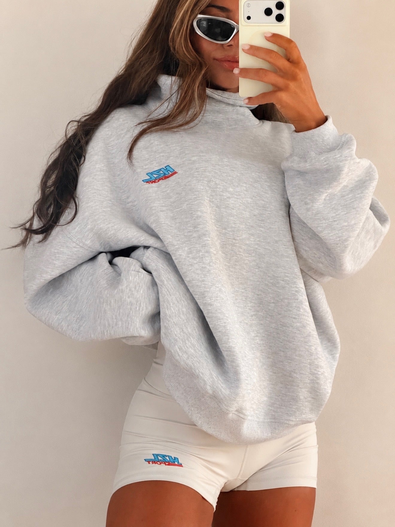 Woman wearing a casual gray oversized sweatshirt and cream sporty shorts with a small logo on the thigh.