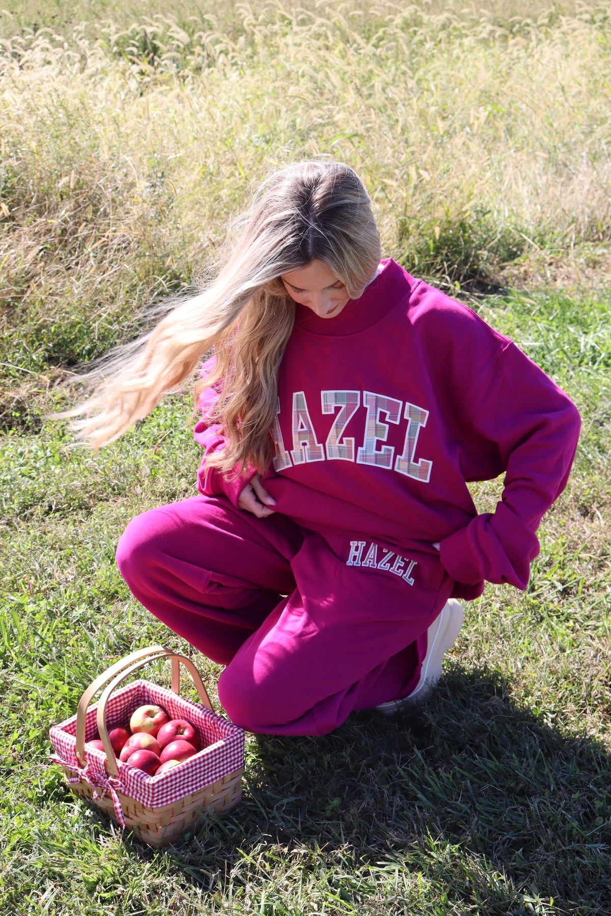 Woman wearing a magenta HZL mockneck sweatshirt and matching pants beside a basket of apples