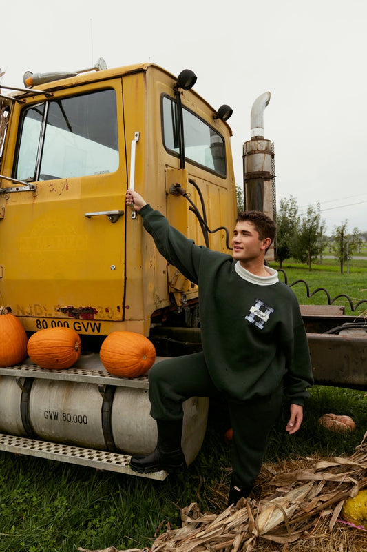 Man wearing green joggers and a sweatshirt beside a yellow truck with pumpkins