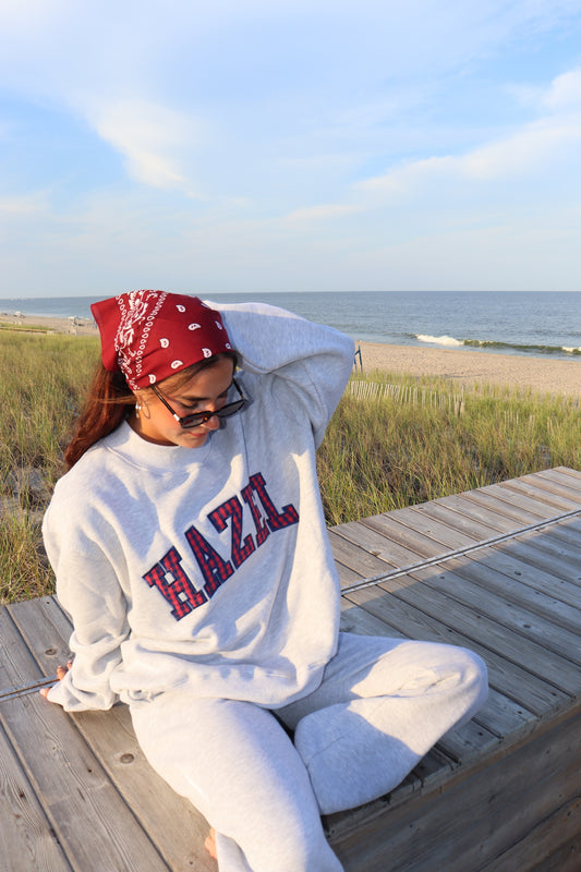 Woman in a gray HZL sweatshirt and matching pants seated on a beach boardwalk beside the ocean