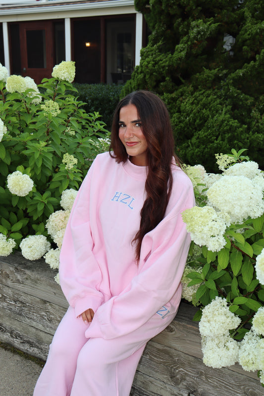 Woman in a pink HZL mockneck sweatshirt and matching pants seated among white hydrangeas
