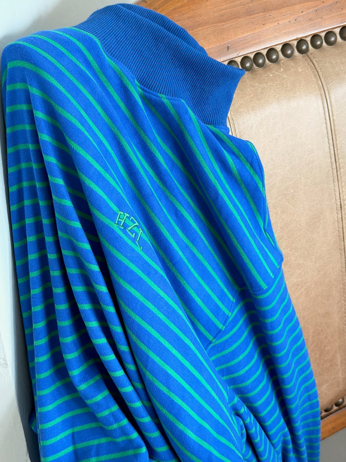 Blue and green striped mockneck sweater with subtle embroidered logo, draped over a leather chair.