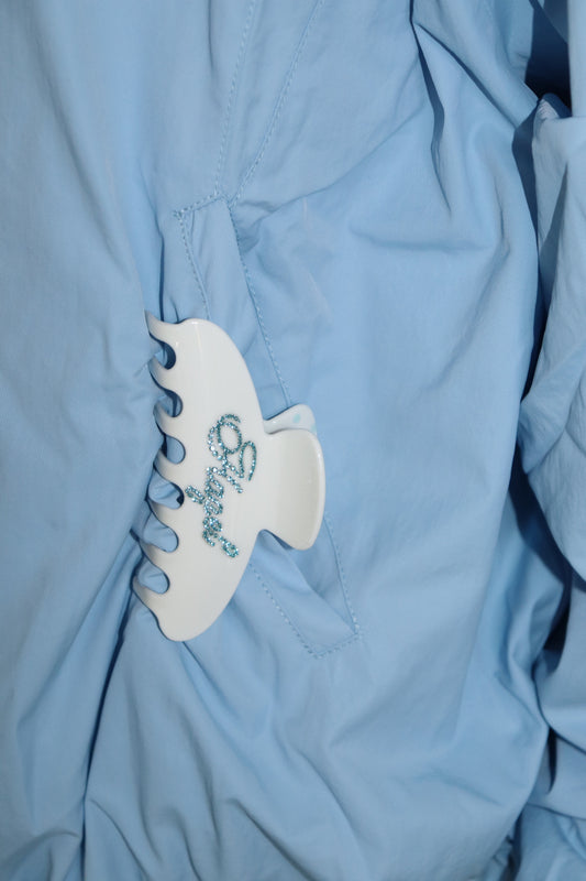 White polka dot claw clip with blue embellishment attached to a light blue jacket