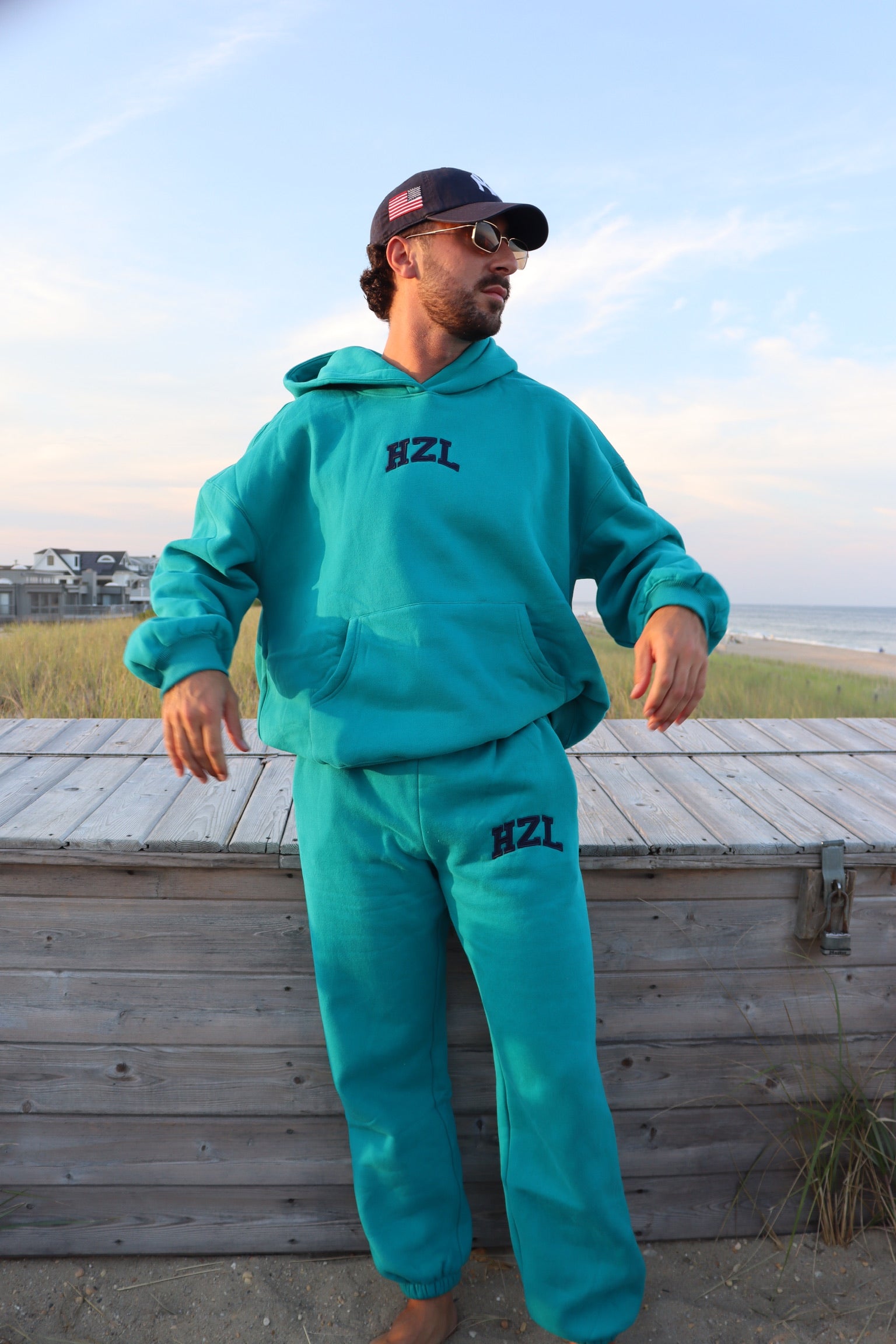 Model wearing a teal HZL hoodie and matching joggers on a beach boardwalk