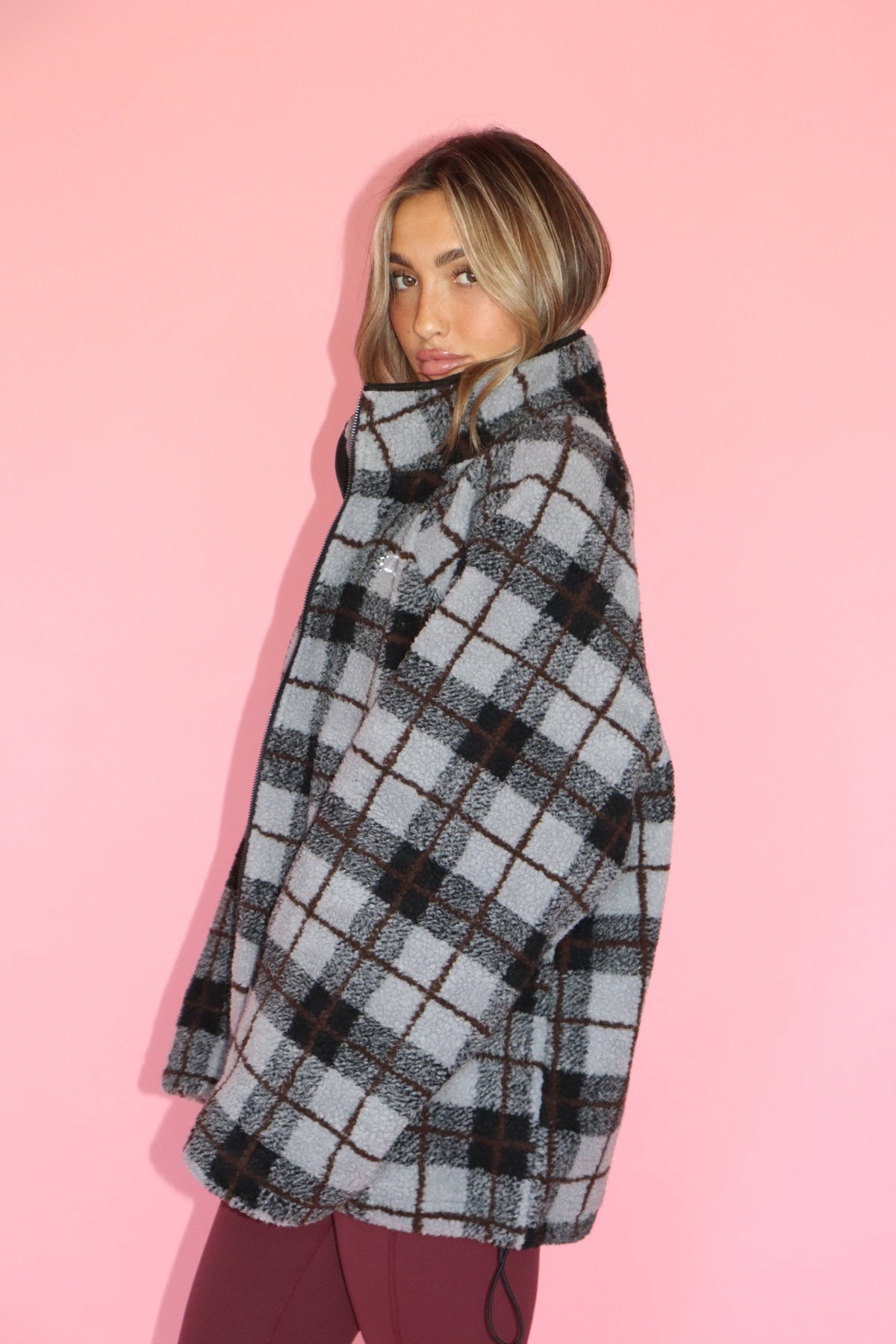 Woman wearing a gray and black plaid fleece jacket against a pink background