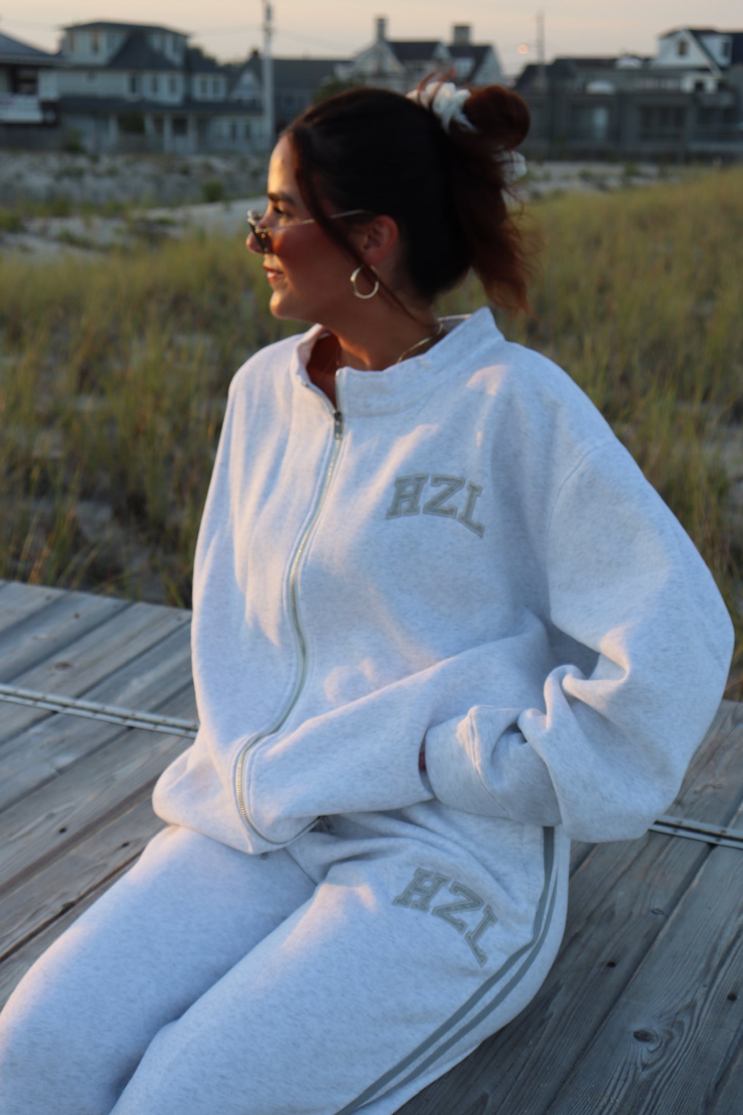 Woman wearing a light gray HZL zip up sweatshirt and matching sweatpants on a beach boardwalk
