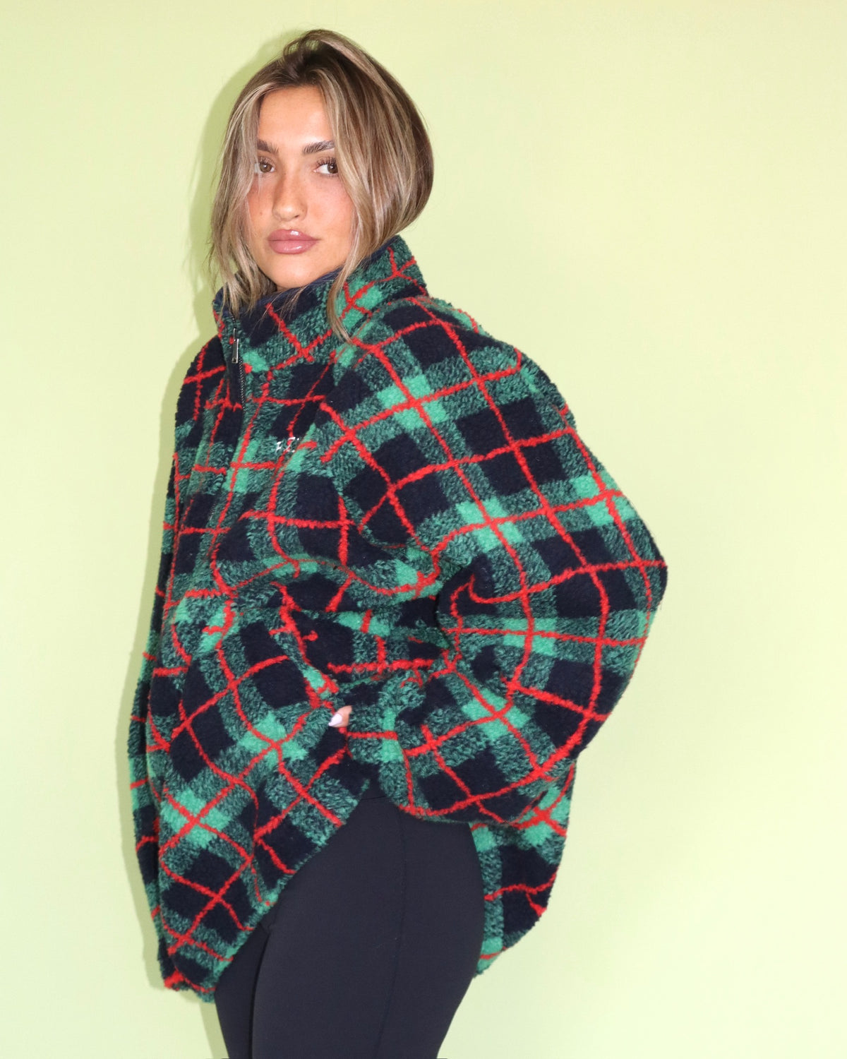 Woman wearing an oversized green red and black plaid fleece pullover with a high collar and black leggings