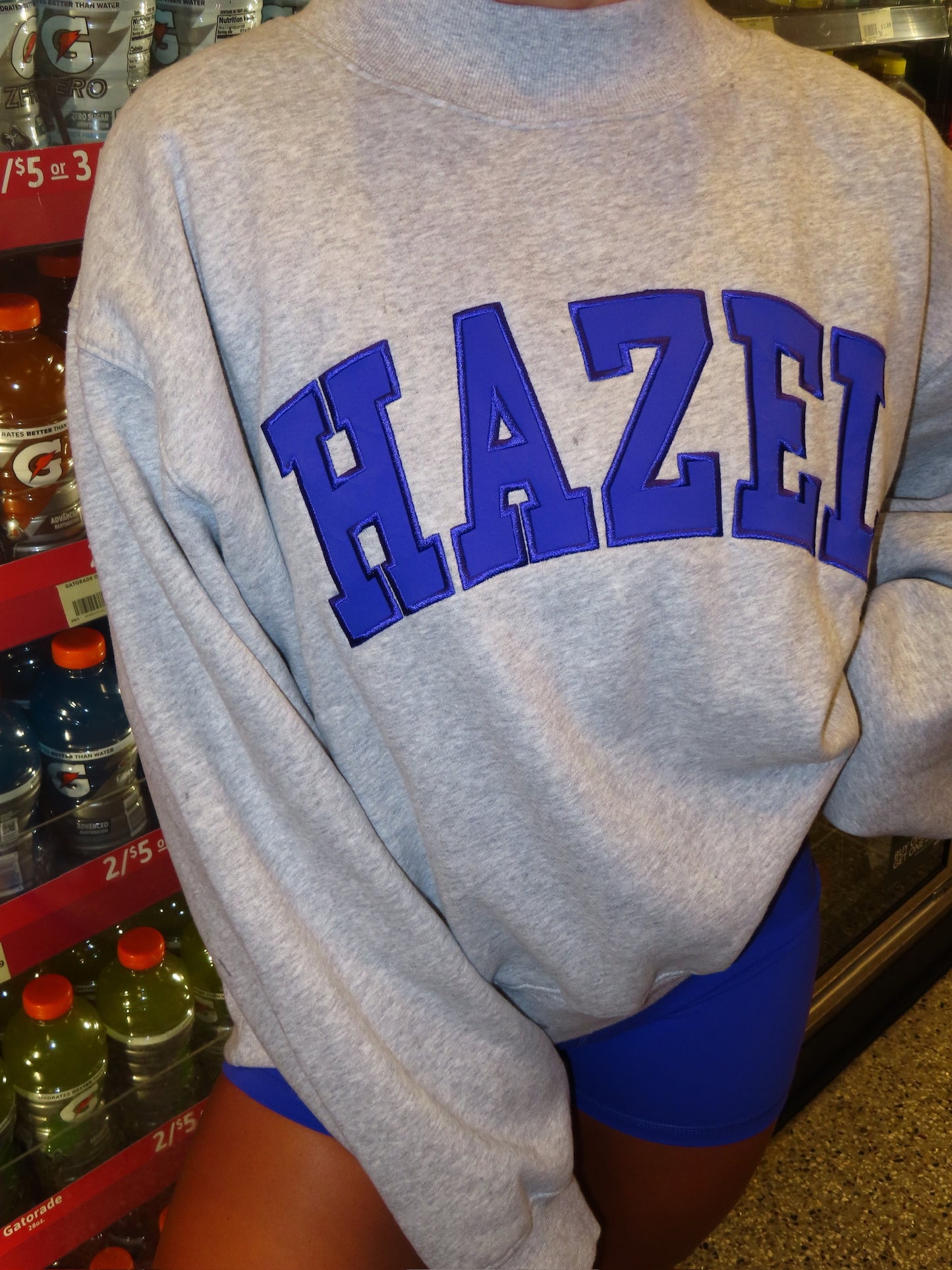 Close-up of a person wearing a gray sweatshirt with bold blue lettering while sitting by a store cooler.