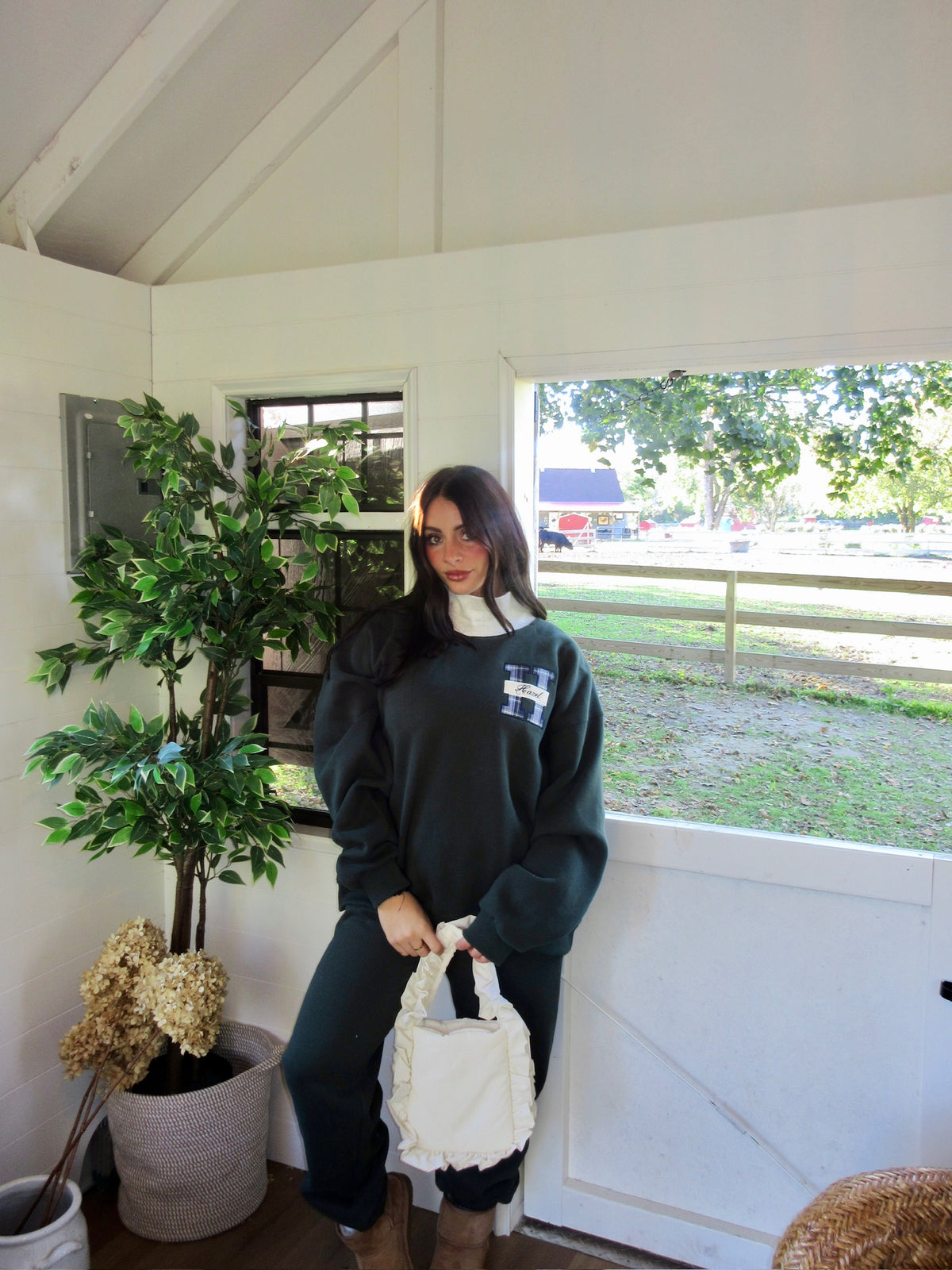 Woman wearing a dark green mockneck sweatshirt with black pants and a cream tote bag indoors
