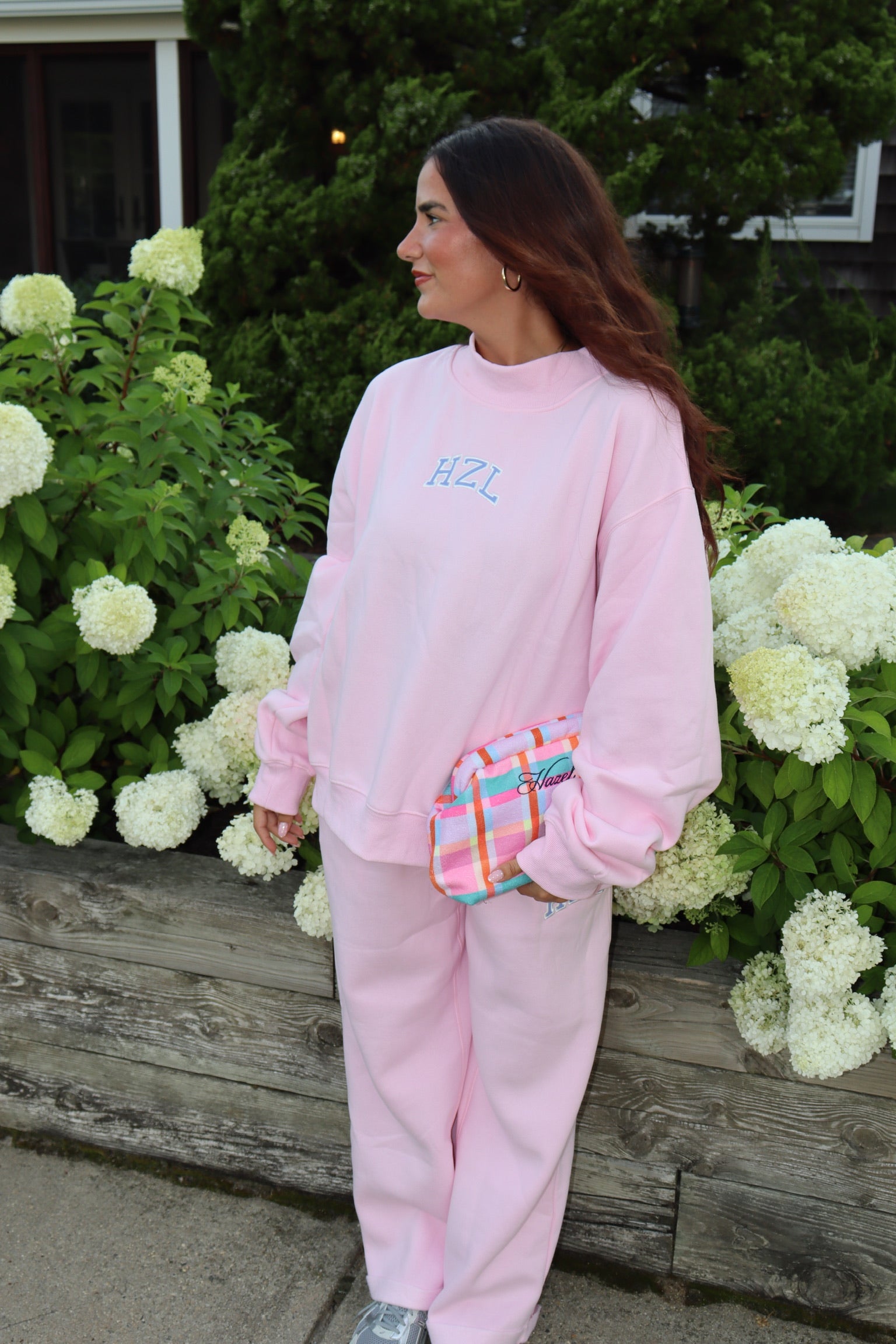 Woman wearing a pink mockneck sweatshirt and matching pants with a colorful waist bag outdoors
