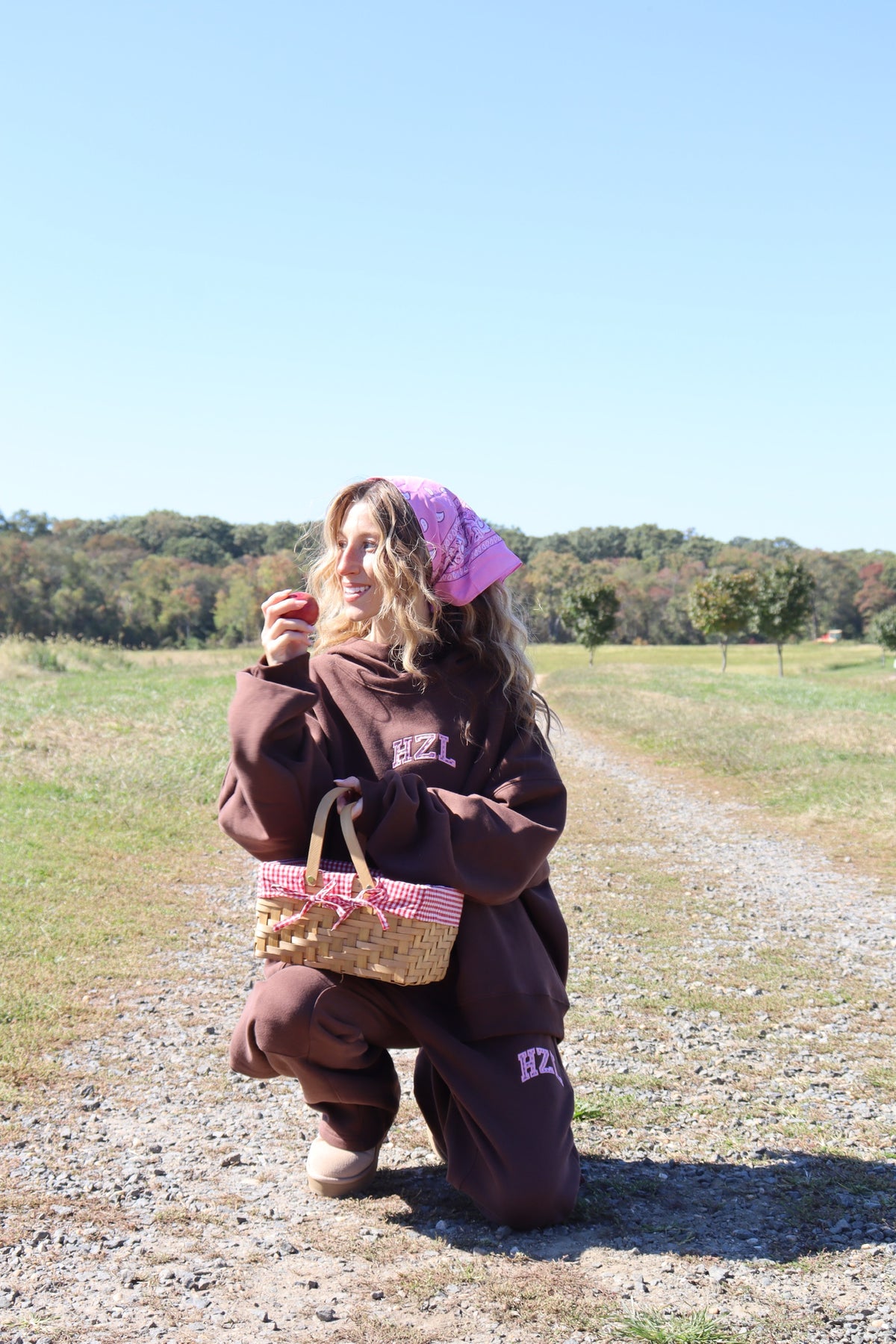 Woman wearing a brown mockneck hoodie and matching pants while kneeling outdoors with a woven basket