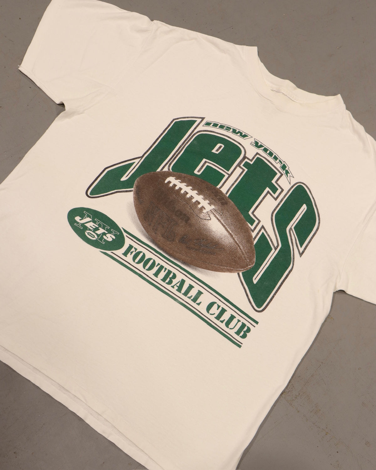 Vintage white football T-shirt with green varsity graphic and brown footballresting on top