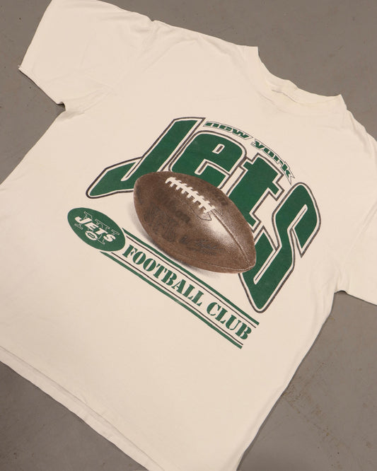 Vintage white football T-shirt with green varsity graphic and brown footballresting on top