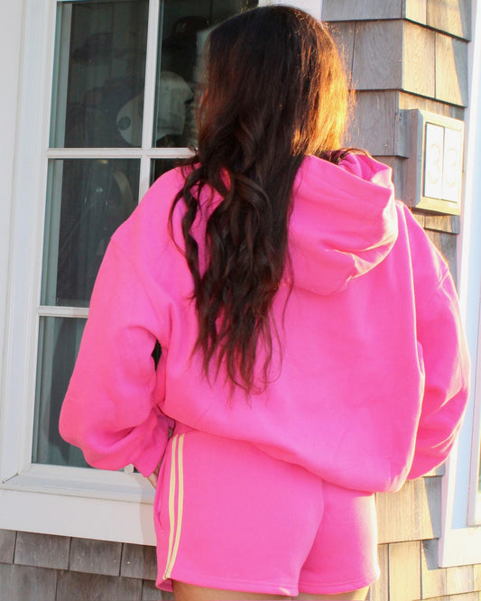 Woman seen from behind wearing bright pink casual shorts with a relaxed pink hoodie in natural light outdoors