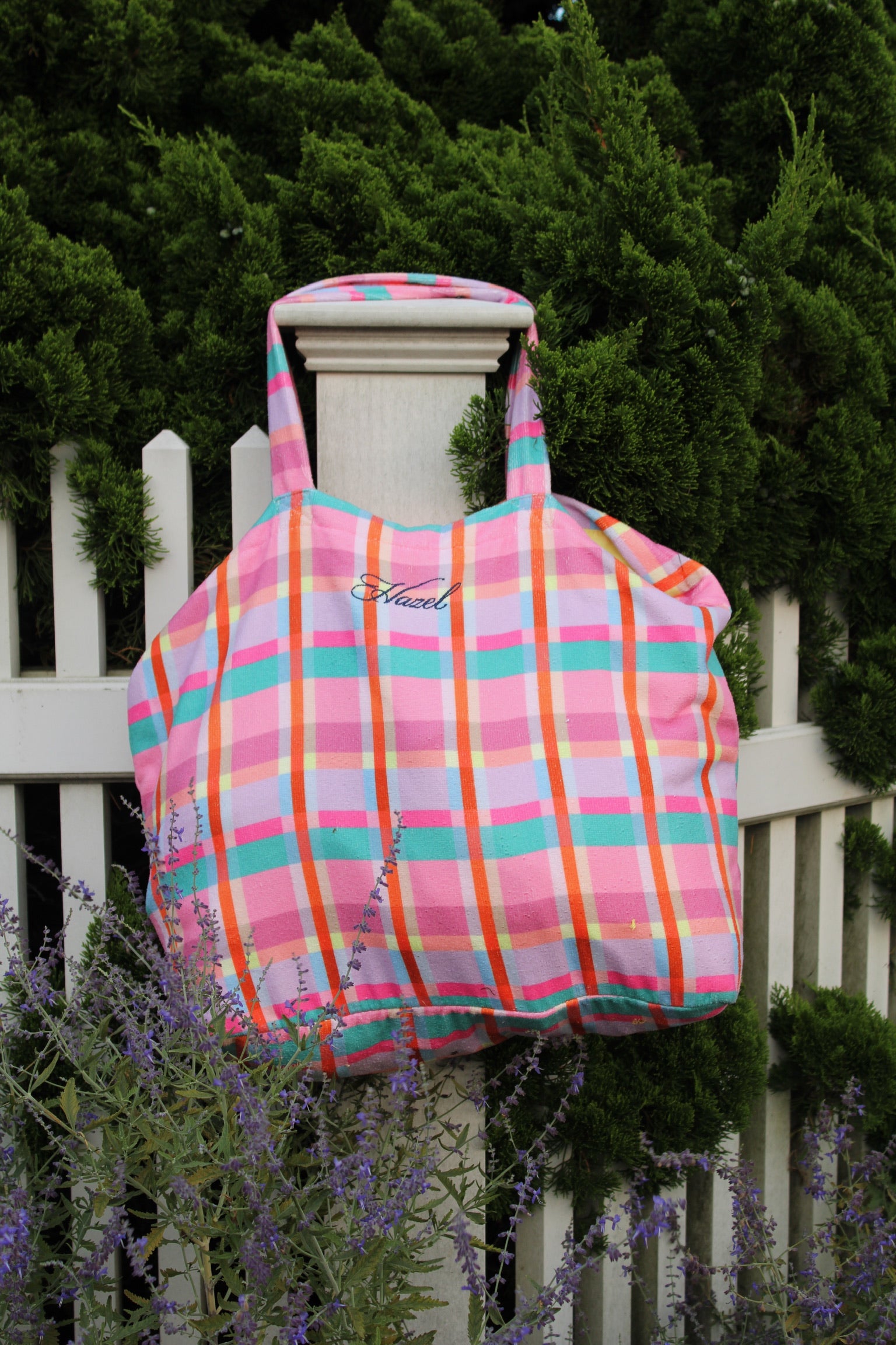 Colorful pink turquoise and orange plaid tote bag hanging on a white garden fence