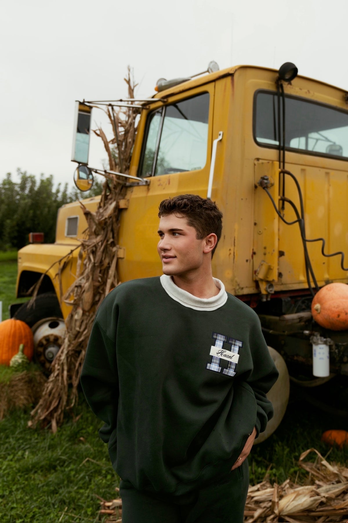 Model wearing a green mockneck sweatshirt in front of a vintage yellow school bus and pumpkins