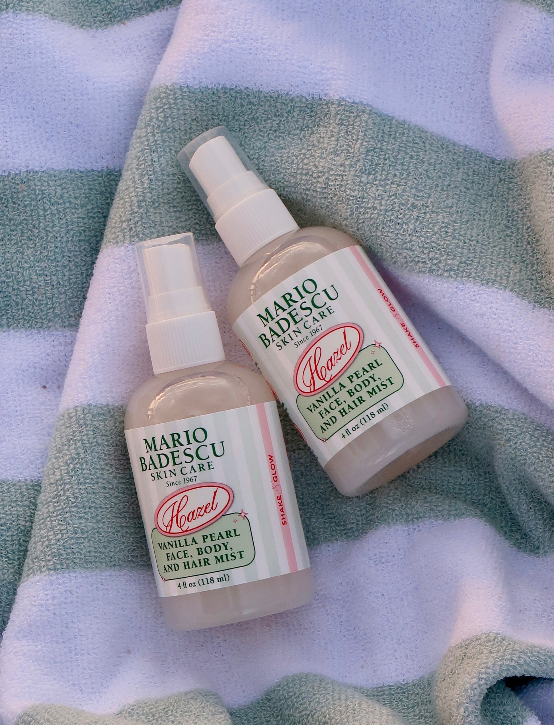 Two bottles of Mario Badescu vanilla pearl face, body, and hair mist on a striped towel background
