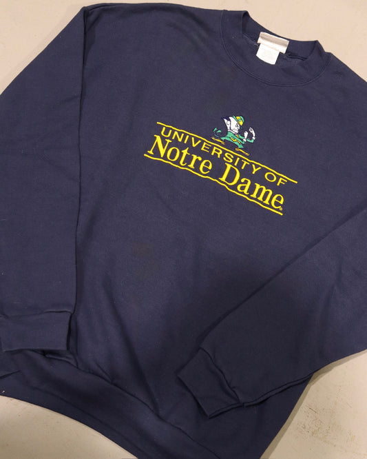 Navy crewneck sweatshirt featuring yellow University of Notre Dame lettering and leprechaun graphic