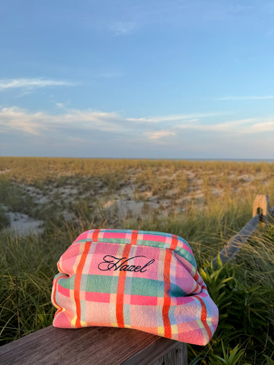 Colorful plaid Hazel clutch resting on a wooden board beside coastal dunes and beach grass
