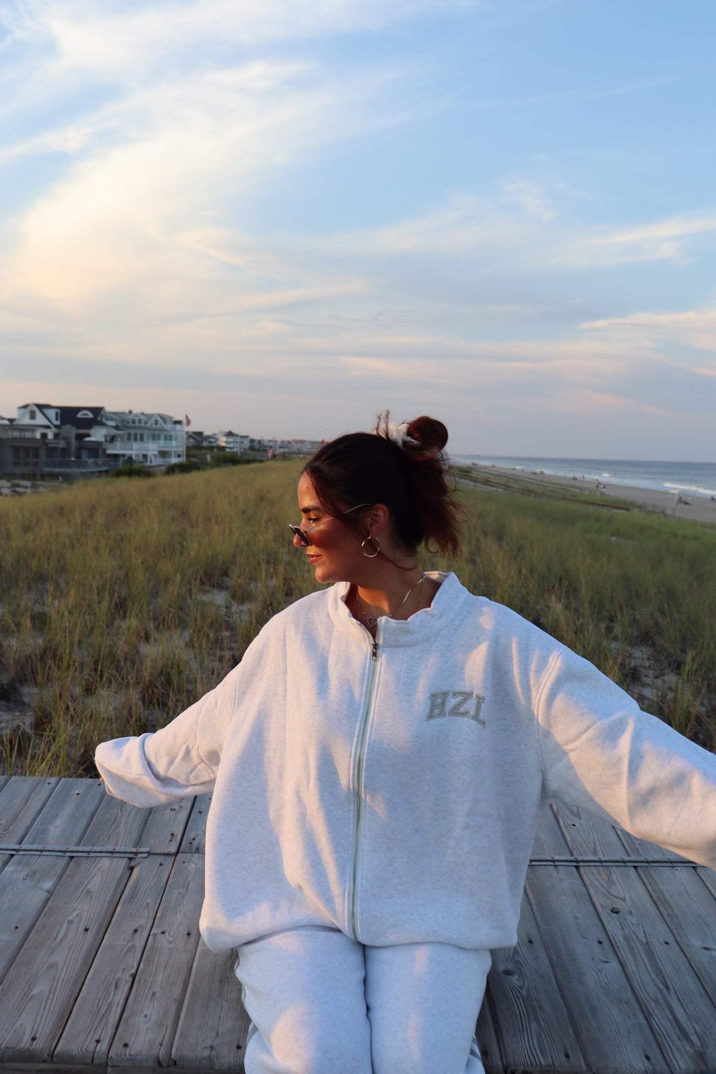 Woman wearing a light gray HZL zip-up sweatshirt and matching pants on a beach boardwalk