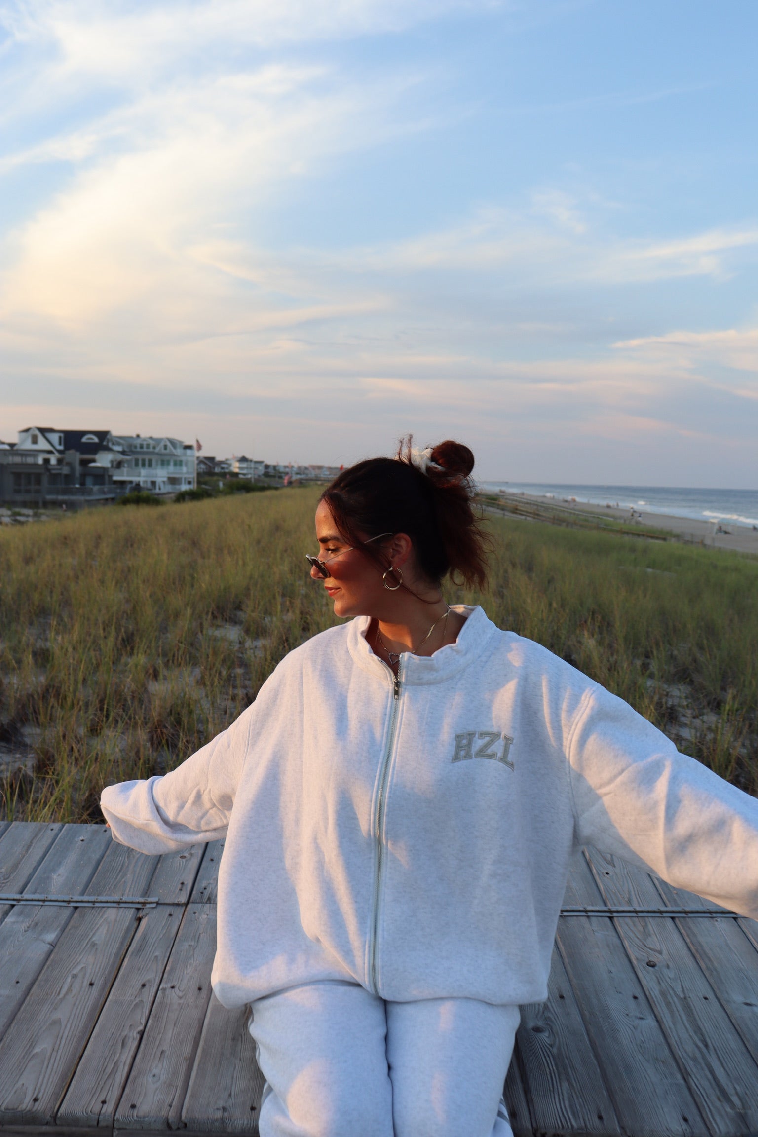 Woman wearing a light gray HZL zip-up sweatshirt and matching pants on a beach boardwalk