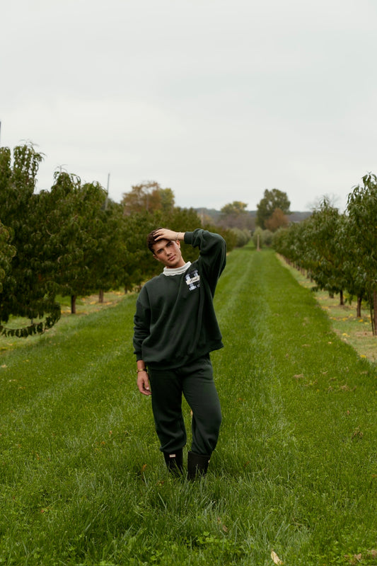 Model wearing green joggers and a matching sweatshirt while standing in a grassy orchard