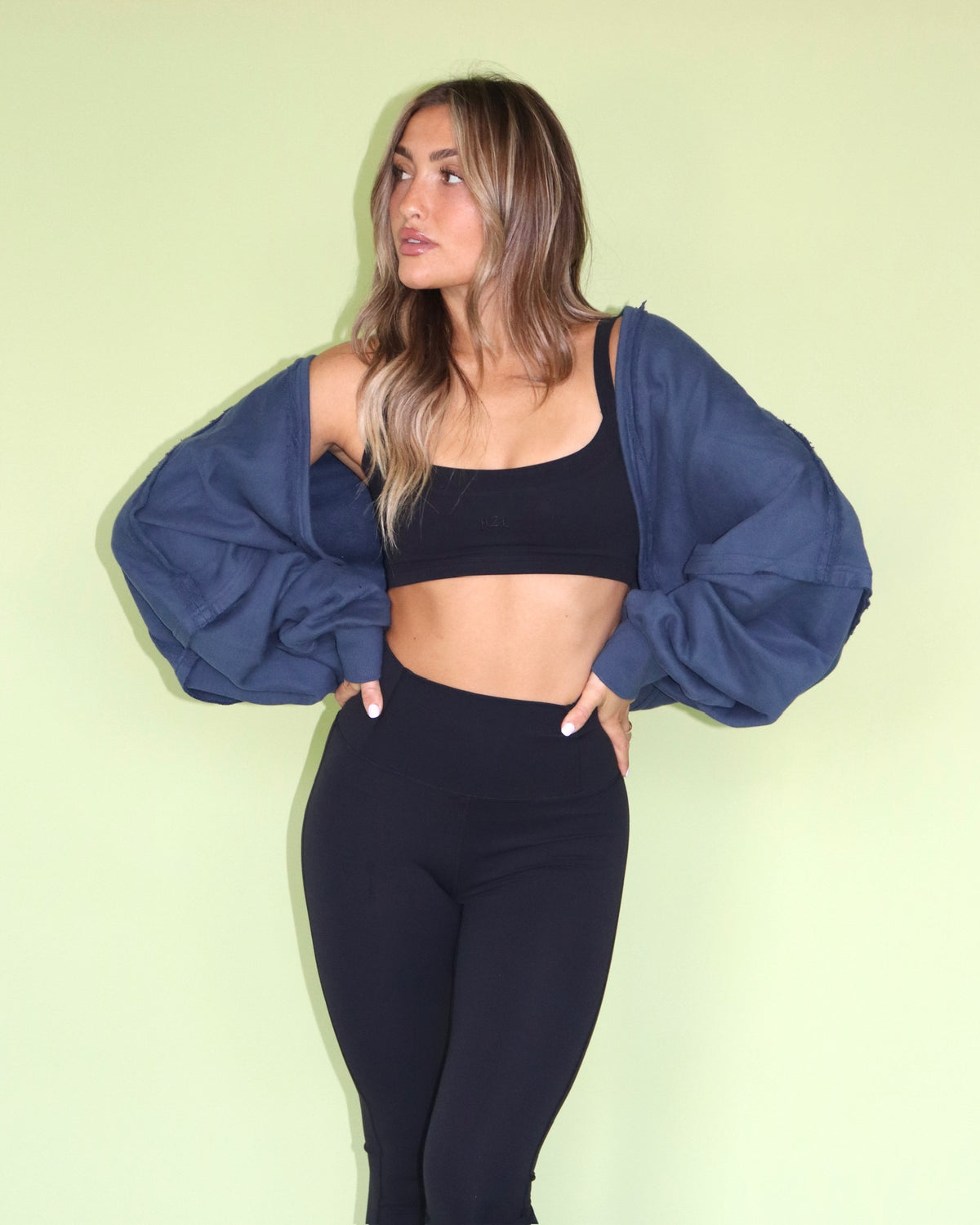 Woman wearing a navy warm up shrug over a black sports bra and leggings