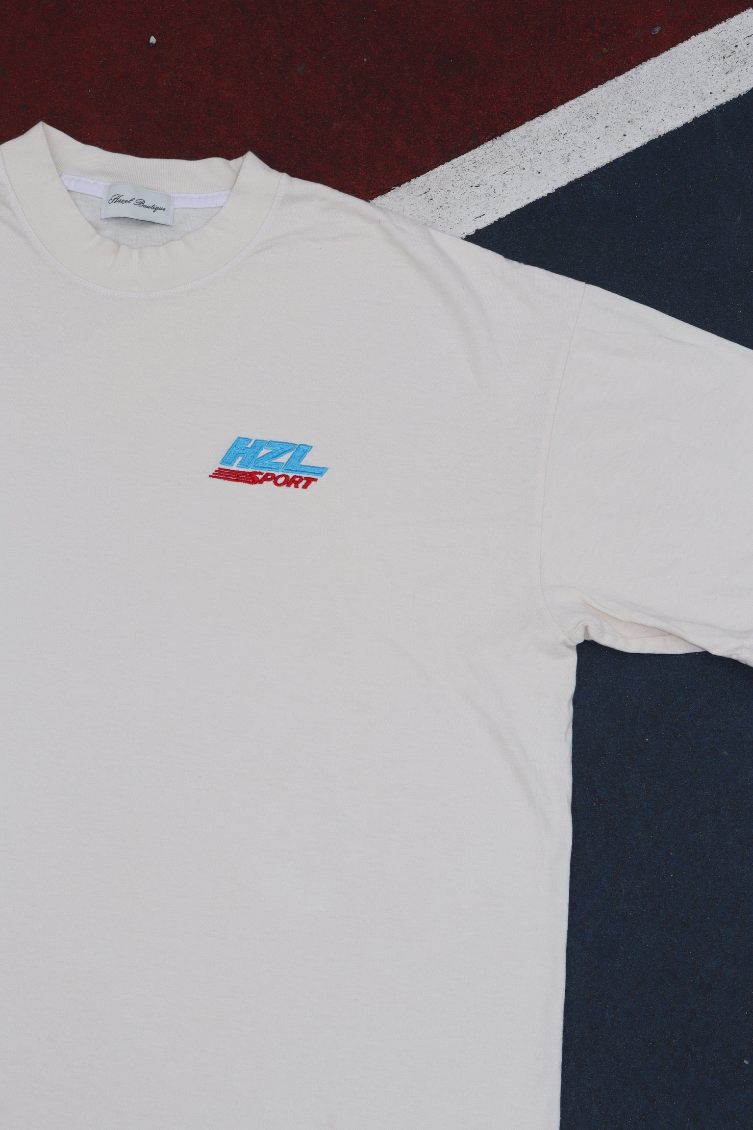 Cream HZL Sport tee shirt laid flat with a colorful logo on the chest