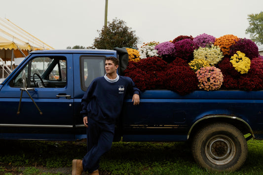 Model wearing navy university joggers while leaning against a blue truck filled with colorful flowers